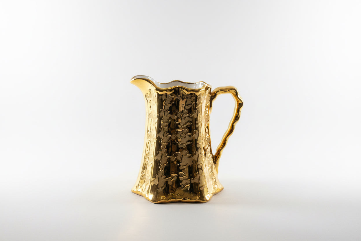 Weeping Gold pitcher by The Vault Creative featuring a sleek, gold-toned design with a curved handle and elegant spout.
