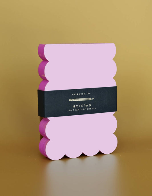 Lilac and hot pink scalloped notepad with a decorative edge, designed by Idlewild Co., placed on a flat surface.
