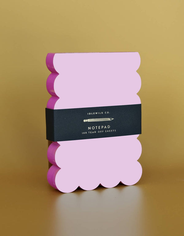 Lilac and hot pink scalloped notepad with a decorative edge, designed by Idlewild Co., placed on a flat surface.