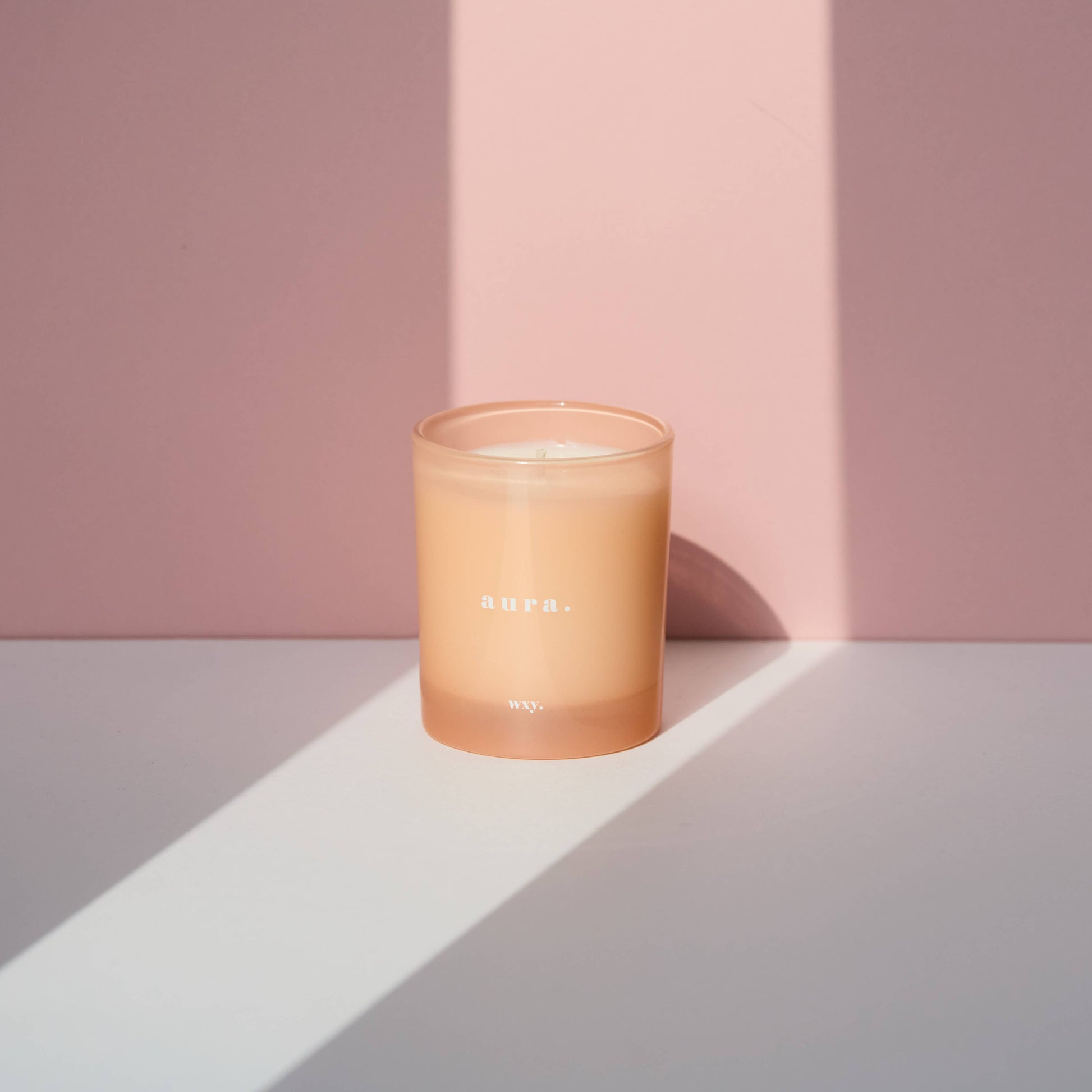 WXY Aura 7oz white woods and amber scented candle in a clear glass jar with a white lid, showcasing a cozy, elegant design