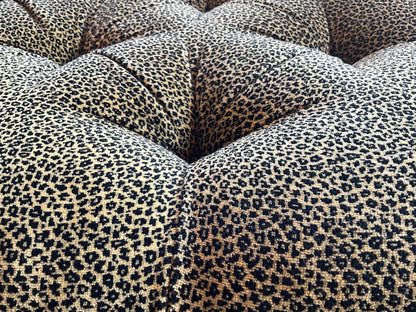 Square leopard print ottoman by The Vault Creative, featuring a plush fabric surface and sturdy wooden legs.