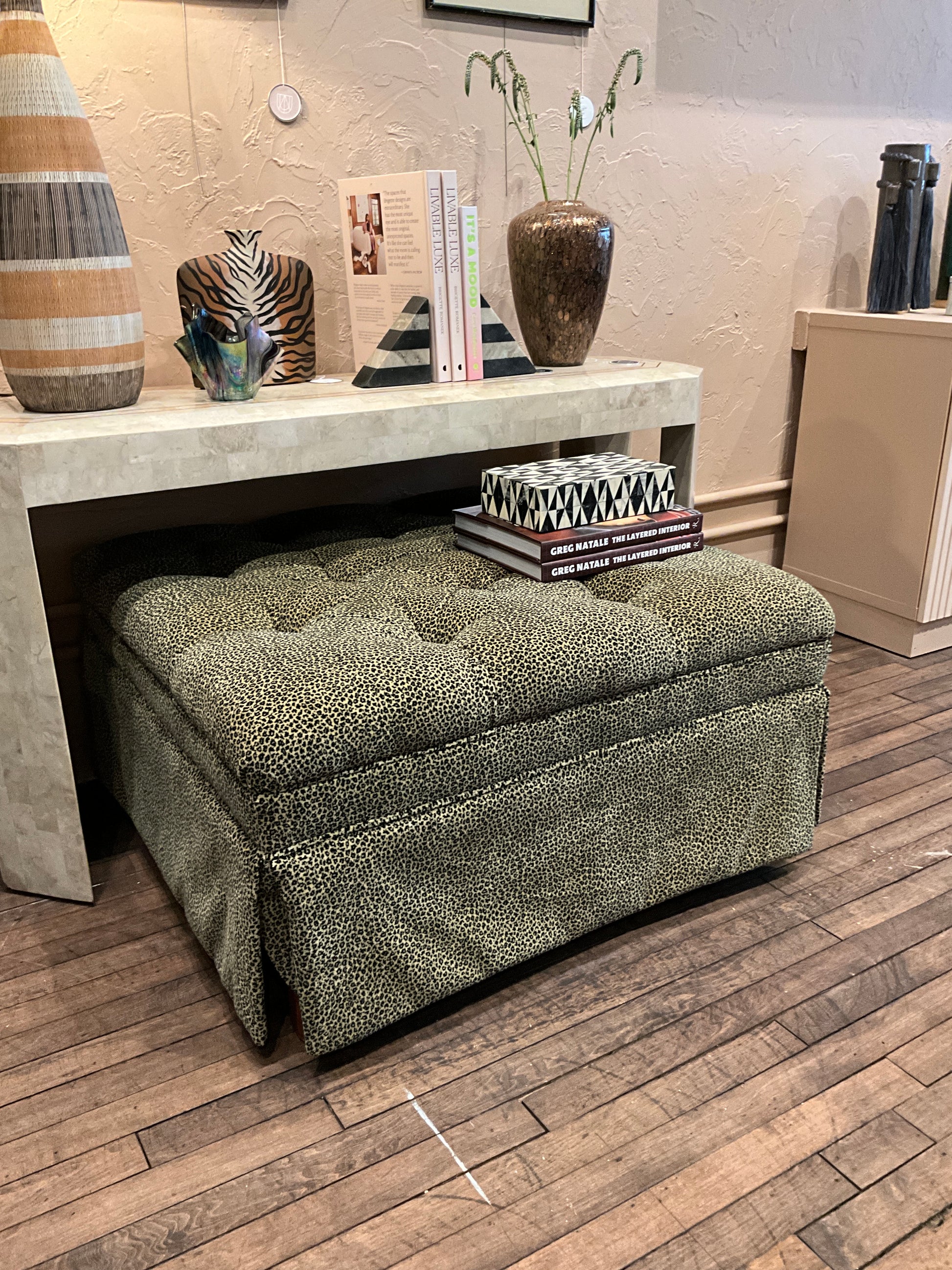 Square leopard-patterned ottoman by The Vault Creative, showcasing a stylish upholstered piece with a bold animal print design.